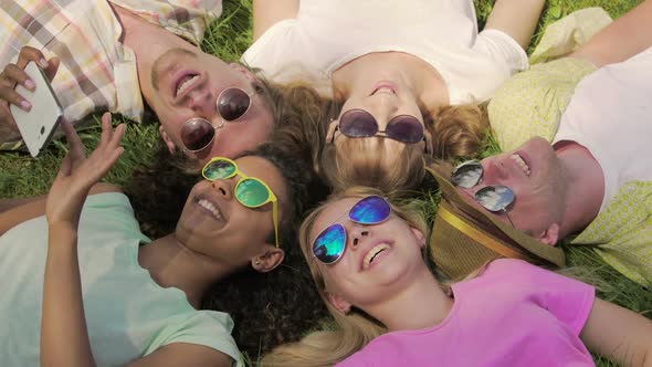 Guys and Girls Watching Funny Video on Phone While Lying on Grass, Happiness