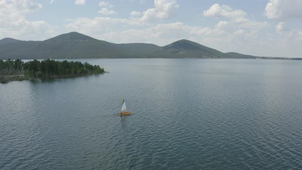 Water surface, sailboat against the background of mountains and pine forest