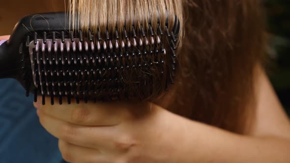 Close-up of a woman brushing and drying her hair Electric hair straightening brush