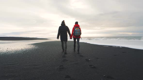 Young Couple Walking on Volcanic Black Sand Beach in Iceland and Having Fun at Sunset Slow Motion