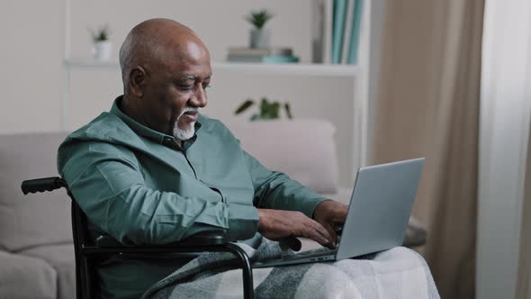 Old 60s African Business Man in Wheelchair Indoor at Home Typing on Laptop Communicates Remotely