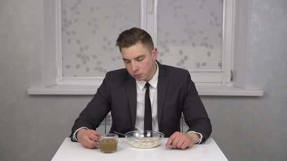 A Sleepy Young Man in a Suit Eats Cereal and Drinks Coffee and is Invigorated