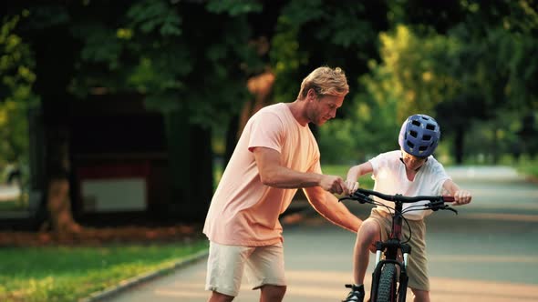 A handsome father is teaching his son to ride a bicycle