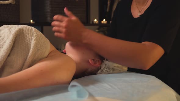 A Young Woman Enjoys a Facial Massage on the Massage Table in the Spa Salon