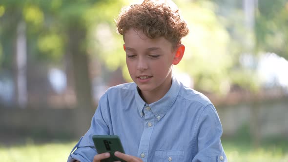 Happy Young Boy Talking on Cellphone Outdoors in Summer Park