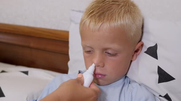 A Caring Mother Sprays Her Son's Nose with Nasal Spray at Home in Bed