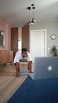 AfricanAmerican Man Practicing Burpee Exercise at Home Doing Pushups and Jumping Using Laptop