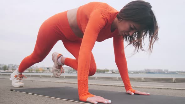 A beautiful girl is doing a running board on a fitness mat outdoors. Athletic woman doing climbing w