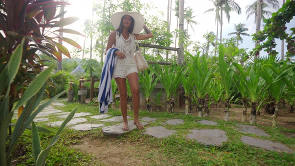 Woman In Sun Hat Walking With Beach Towel On Resort Path