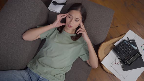 Top View Portrait of Overburdened Exhausted Young Asian Woman Lying on Couch Rubbing Temples