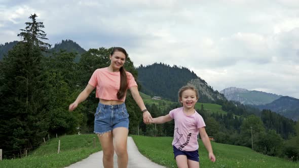 Young Woman with Her Little Daughter Is Running Through a Picturesque Mountainous Area. Wonderful