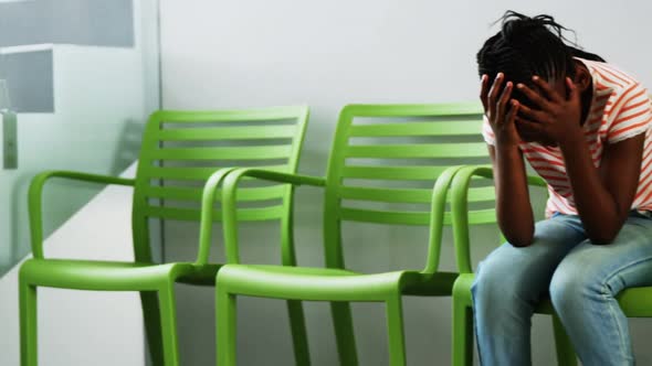 Upset girl sitting on chair in hospital corridor