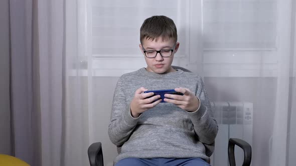 Smart Boy in Glasses Watching a Video in a Mobile App on a Smartphone