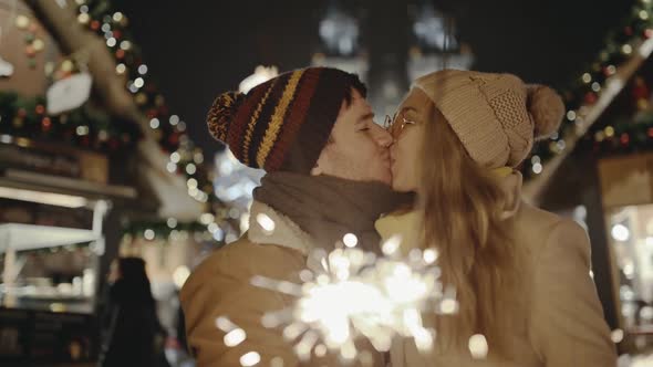 Charming Couple in Love Kissing and Burning Bengal Lights at Festive European Street Fair