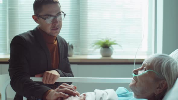 Man Supporting Senior Mother in Hospital Ward