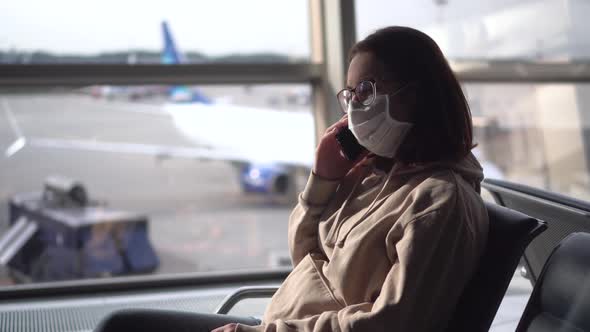 A Young Woman Sits and Speaks on the Phone Against the Background of a Window at the Airport