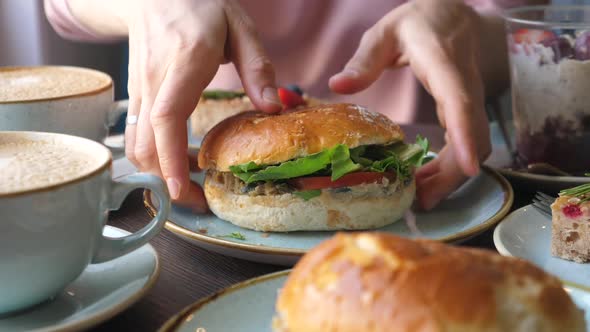 Female Hands Take a Burger From a Plate in a Cafe.