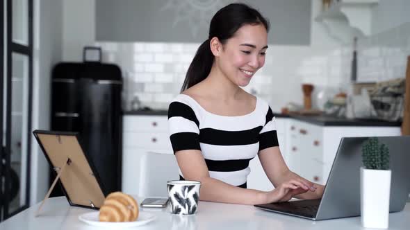 Smiling young woman sitting on chair using laptop notebook looking at screen typing message