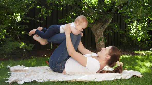 Smiling Mother Lifting Up and Rocking Her Little Baby Son in Garden