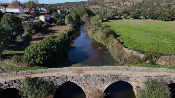 Drone flies over  Roman bridge next to a small river town in Portugal.