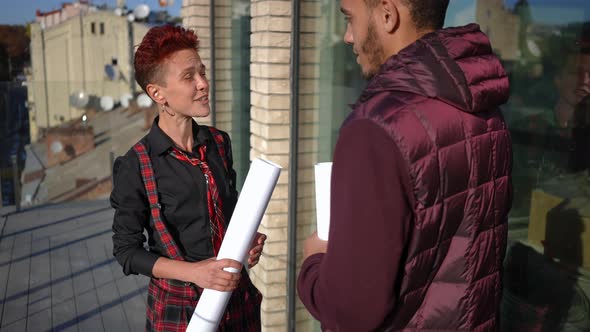 Redhead Pierced Caucasian Woman Talking to African American Man Standing in Sunshine on Terrace