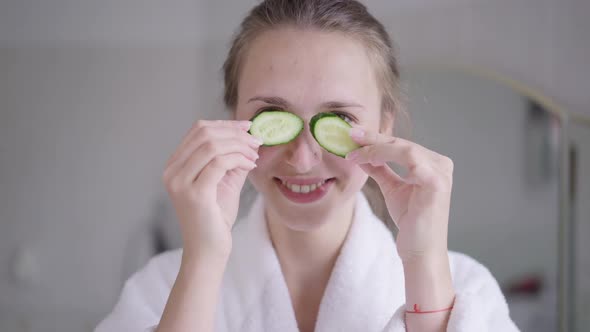 Cheerful Beautiful Young Woman with Toothy Smile Having Fun Playing with Cucumber Slices Over Eyes