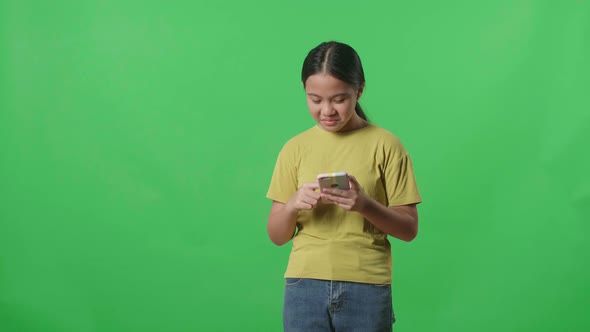 Asian Kid Girl Emotionally Flipping Something On The Phone While Standing In The Green Screen Studio