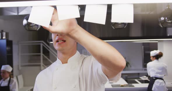 Caucasian male chef working in a restaurant kitchen checking orders, with colleagues working