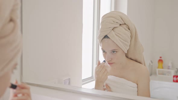 Teenage girl applying makeup in front of the bathroom mirror