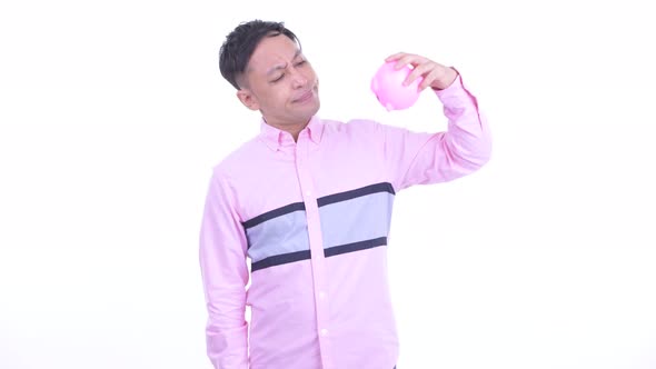 Stressed Japanese Businessman Holding Piggy Bank and Giving Thumbs Down