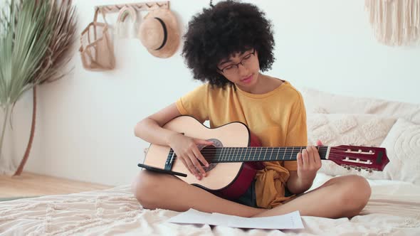 Afro American Girl in a Yellow Tshirt Learns to Play the Guitar Using a Smartphone