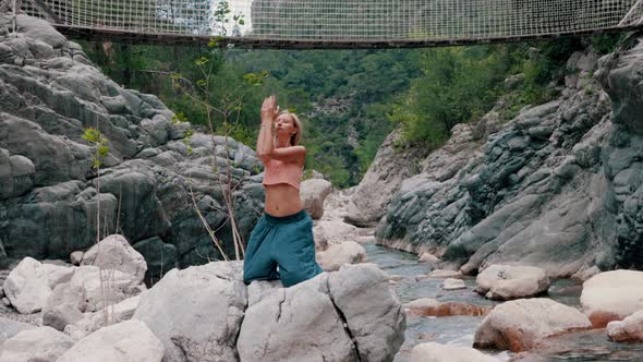 A Blonde Woman Does Meditative Exercises Standing with Her Knees on the Rock in the Middle of the