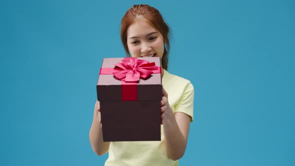 Young Asia girl smile and holding opened present box isolated over blue background.