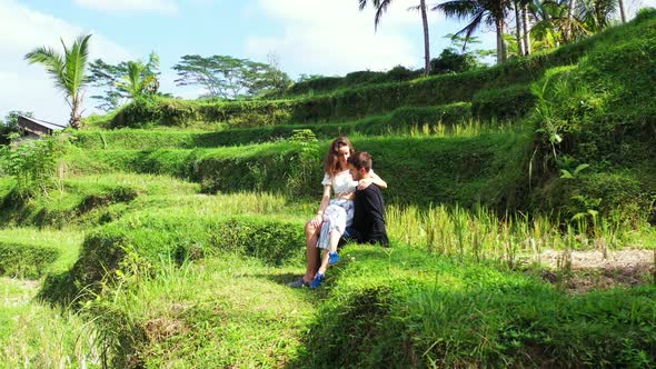 Girlfriend is sitting on the boy's lap, watching him on eyes, talking about beautiful green landscap