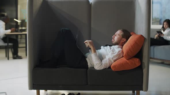 Businessman Lies in a Large Chair and Works at a Laptop Office Work in an Open Space a Man Types