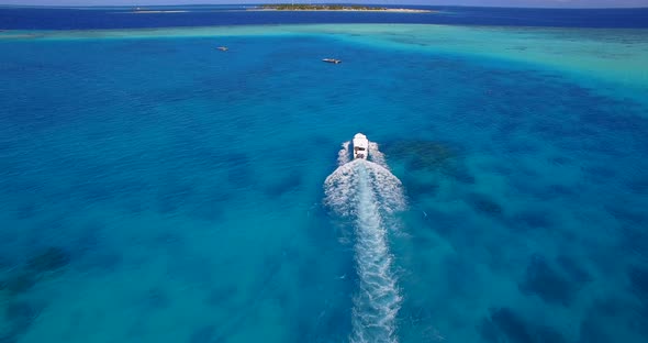 Aerial drone view of a motor boat going to a scenic tropical island in the Maldives