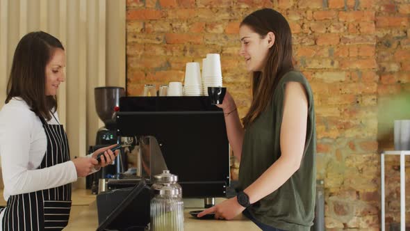 Caucasian waitress receiving contactless payment and giving coffee cup to caucasian female customer