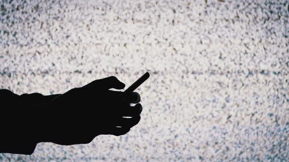 Silhouette of a Hand Holding a Smartphone on TV Screen Background with White Static Noise