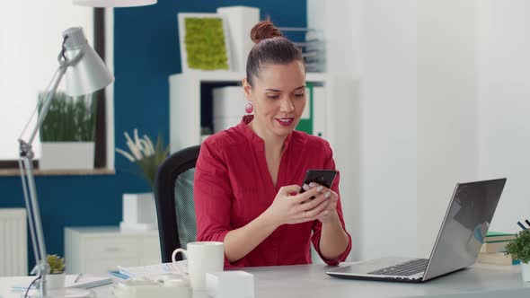 Sales Consultant Browsing Internet on Smartphone at Desk