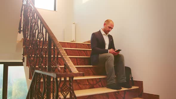 Businessman Typing on Smartphone Sitting on Stairs