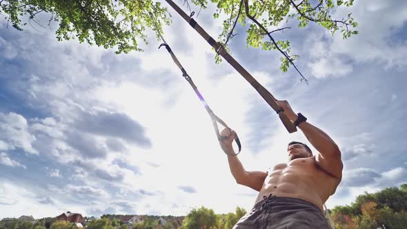 Man is engaged in trx exercises under the sky.