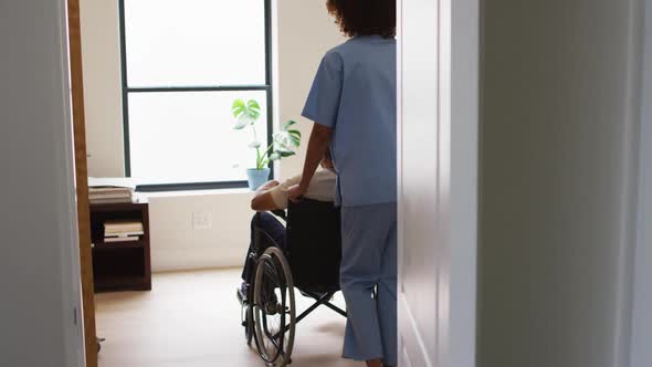 Mixed race female doctor assisting senior man in wheelchair at home