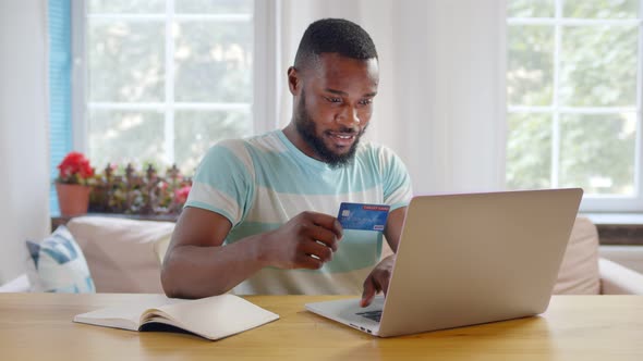 African Young Man Using Laptop and Credit Card Paying Bills Online