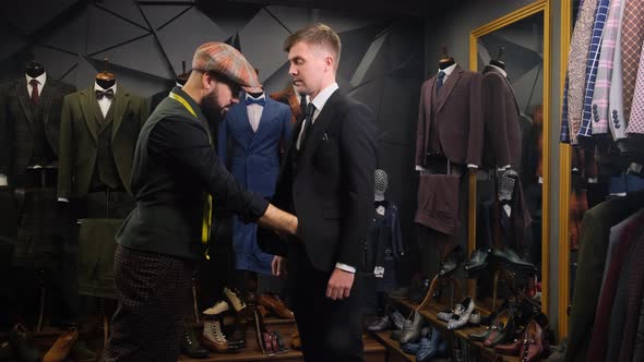 A Bearded Tailor Dresses a Handsome Young Man in a Quality Handmade Suit in an Atelier, Creative