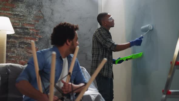 Cheerful AfricanAmerican Man Paints Wall Talking to Brother