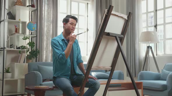 Side View Of An Asian Artist Man Thinking Before Painting On The Canvas