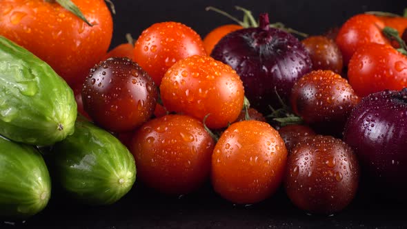 Cherry tomatoes, cucumbers, avocado and red onion on a black background in water drops.