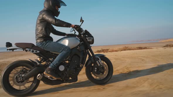 Motorcyclist Driving His Customized Fast Motorbike on the Dirt Road in Desert Around Sea or Lake