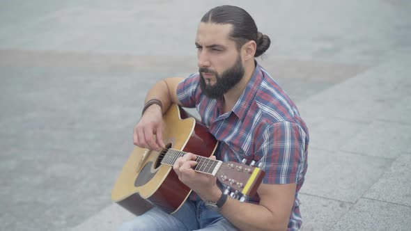 Middle Shot of Focused Caucasian Guitarist Playing Muscial Instrument Outdoors. Portrait of