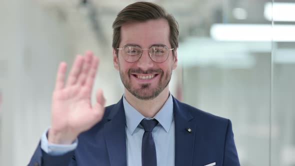 Portrait of Cheerful Young Businessman Waving at the Camera 